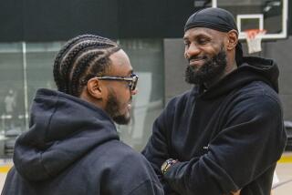 Bronny and LeBron James smile while standing and looking at each another on the court at the Lakers practice facility