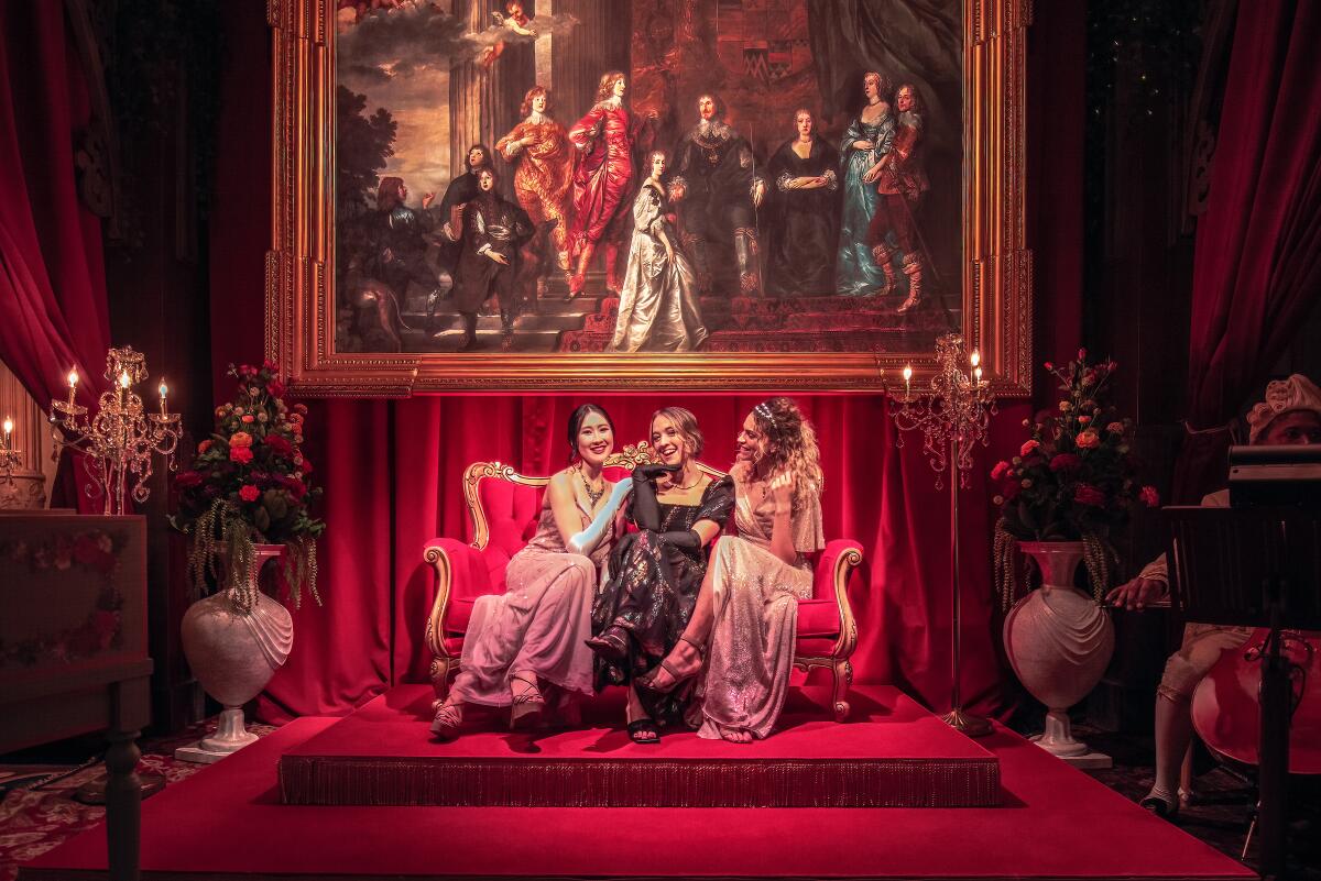 Three women in evening gowns on a couch in a Regency parlor.