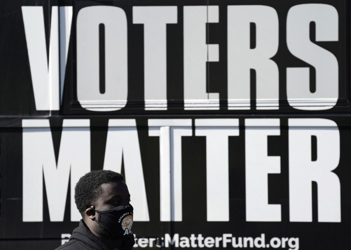 A man stands in front of a Black Voters Matter sign. 