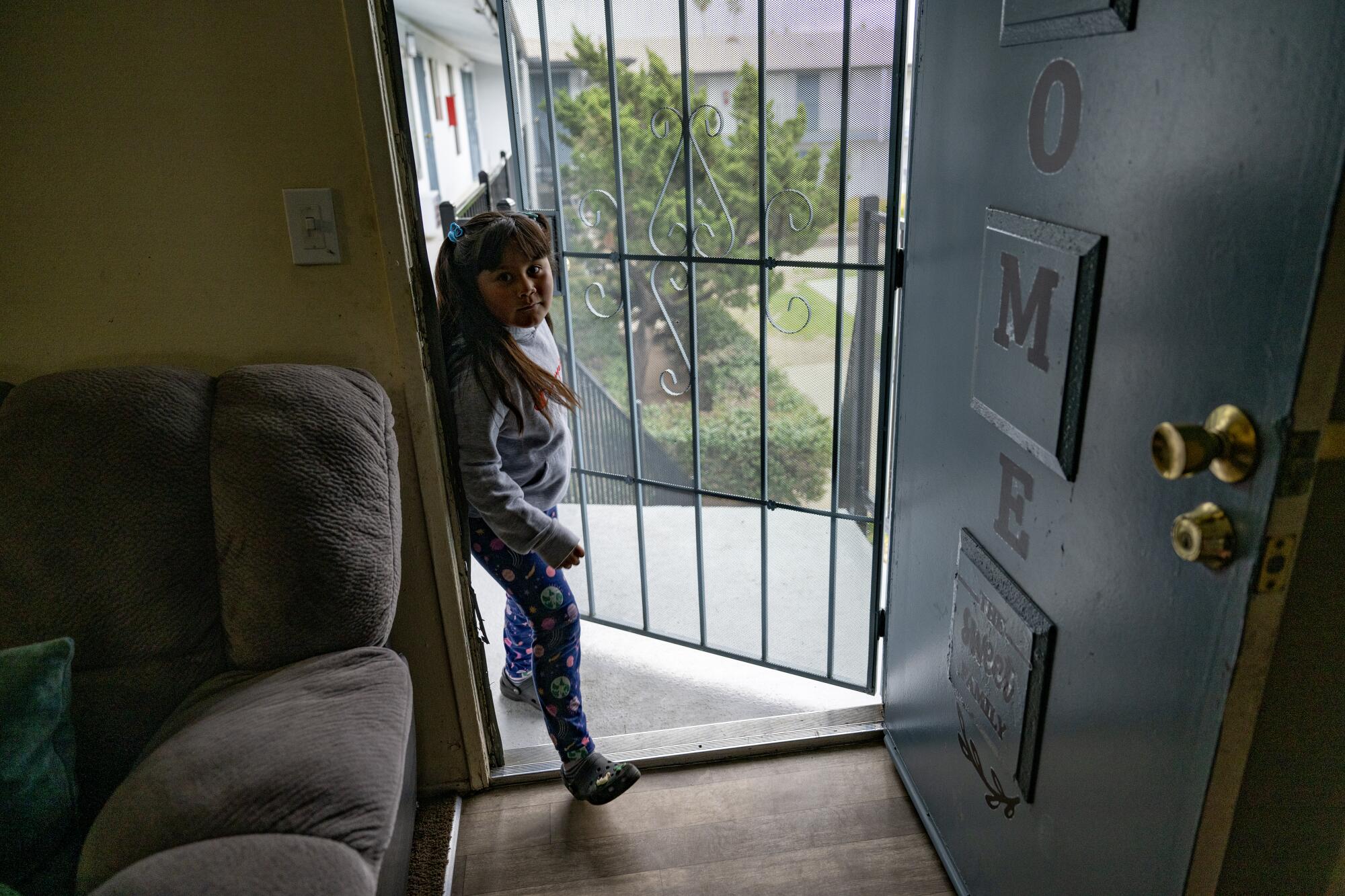 A girl enters an apartment through a screen door.