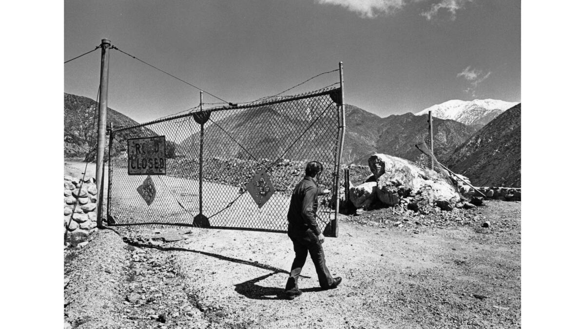 A man opens a large chain link gate on a dirt road