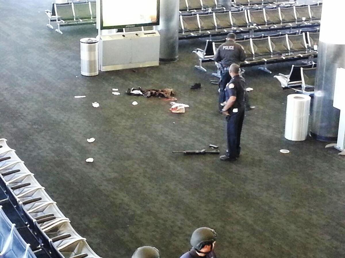 Police officers stand near an assault-style rifle in Terminal 3 of Los Angeles International Airport where a gunman opened fire on Nov. 1, killing one person and wounding three others.
