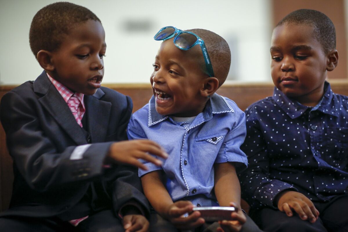 Ryan Labady, 5, Joshua Valsaint, 4, and Ruben Jacques, 4 from left, talk about playing the harmonica, in Joshua's hands, during a service at Christ United Methodist Church. (Jay L. Clendenin / Los Angeles Times)