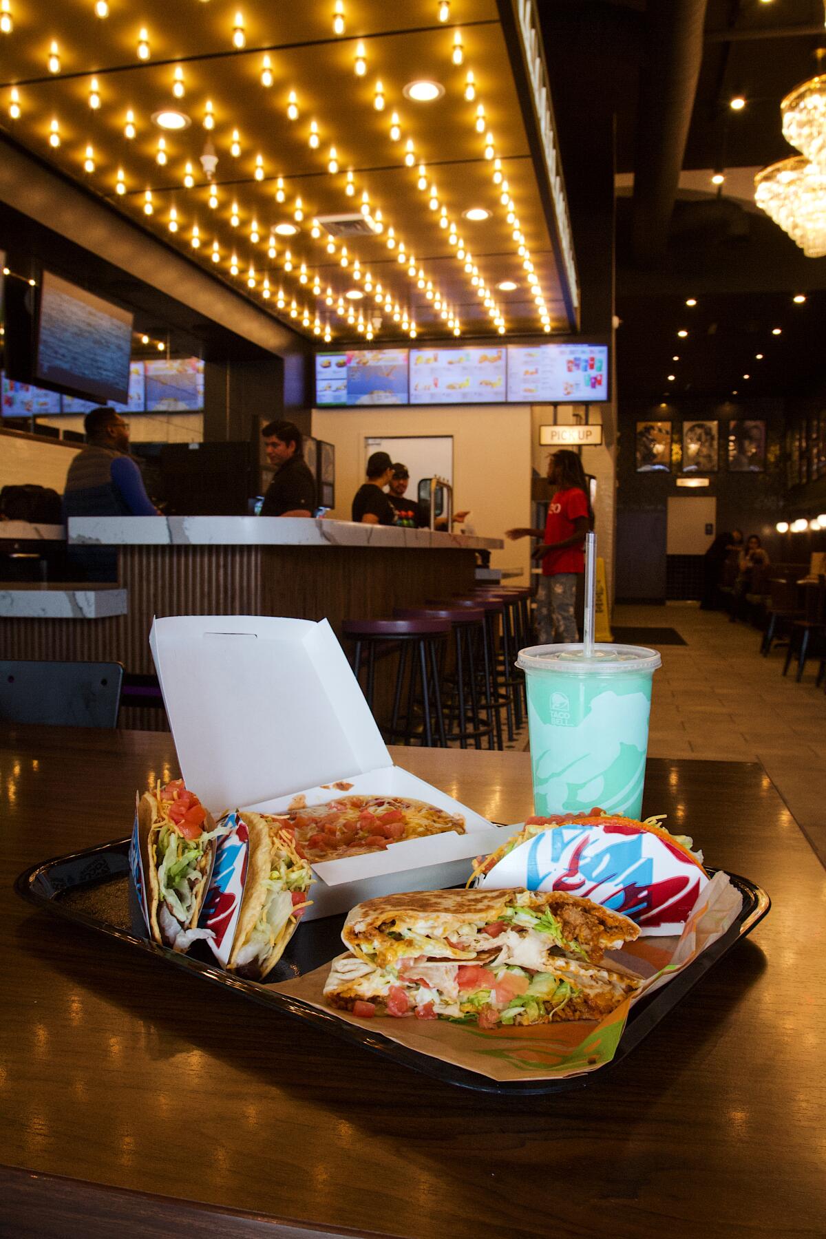 A vertical photo of a tray of food and a Baja Blast slushie on a tray in the foreground; behind is the bar and faux marquee.