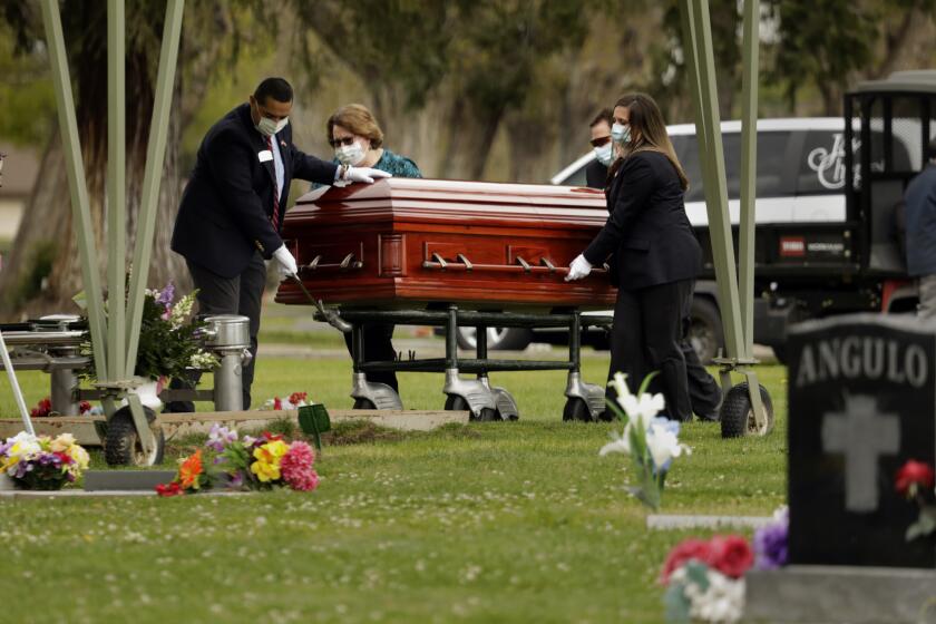 MADERA, CALIFORNIA-APRIL 8, 2020-Wanda DeSelle, age 76, died of Covid 19 on April 3, 2020, in the town of Madera, California, where she worked in a medical office. Wearing masks and gloves, funeral director Sarah Smith, far right, and other members of Jay Chapel Funeral Home bring the body to the gravesite. Immediate family had to remain in their cars as DeSelle was buried on April 8, 2020. Employees of the funeral home and cemetery workers handled the burial and were the only ones allowed at the gravesite. (Carolyn Cole/Los Angeles Times)