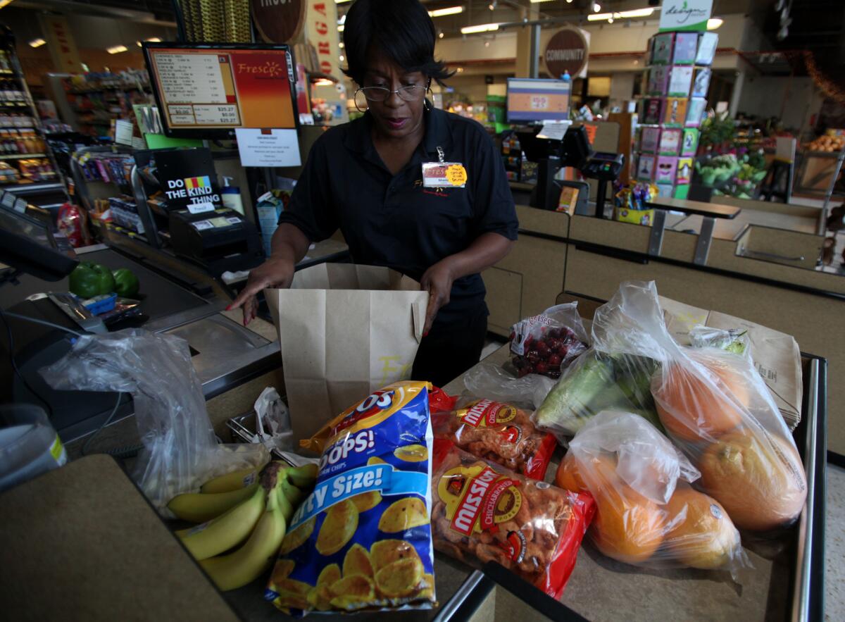 Cashier Sheila Curl puts groceries into a paper bag at Fresco Community Market in Los Angeles last year. Plastic carry-out bags are now banned in Los Angeles and a new bill would ban them statewide.