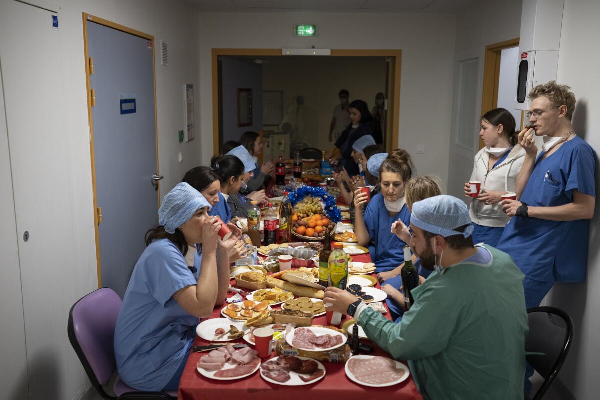 Men and women in hospital scrubs have a meal at a long table set with various dishes 