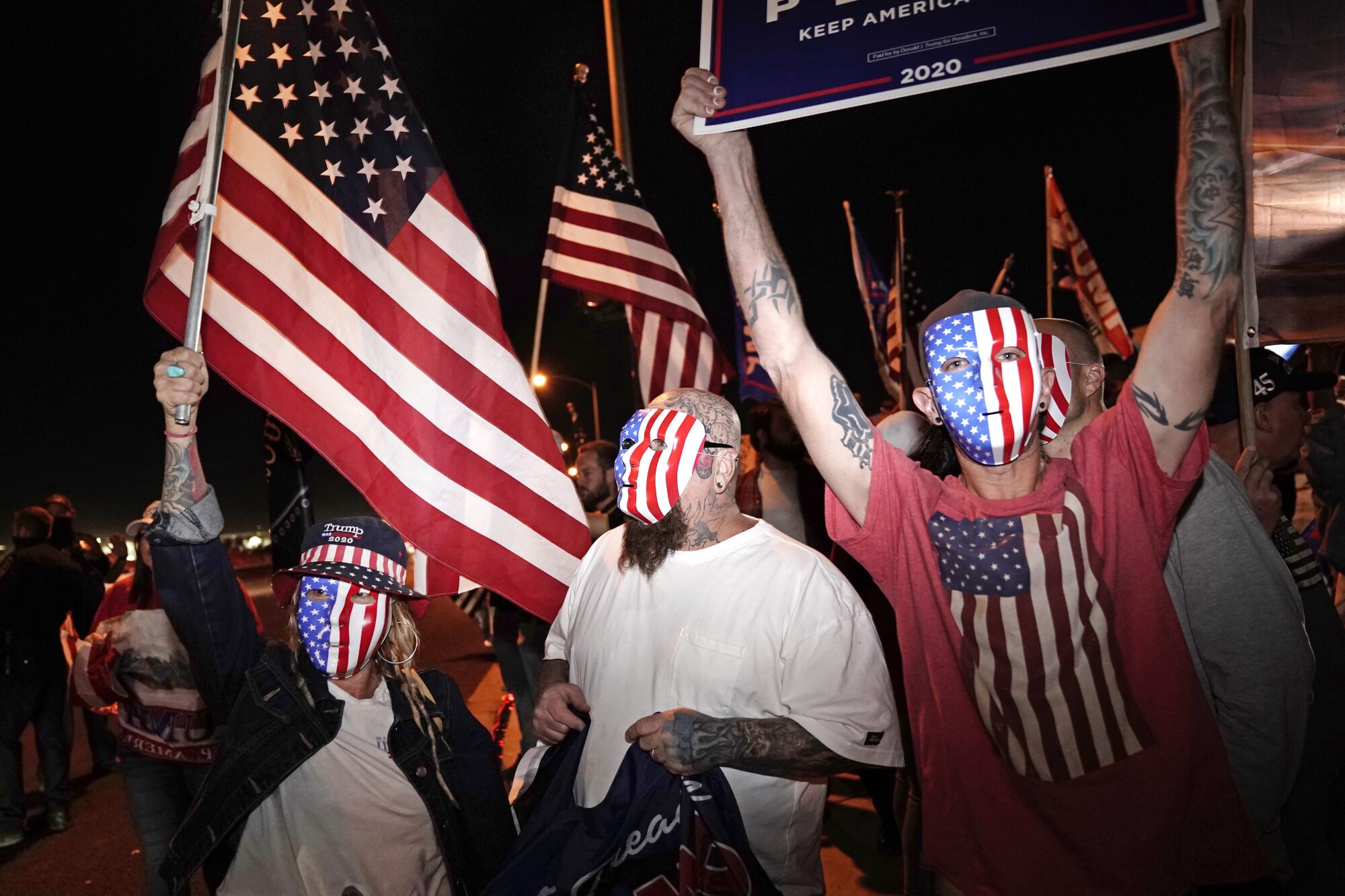 People in U.S. flag masks and Trump gear wave flags and Trump campaign signs