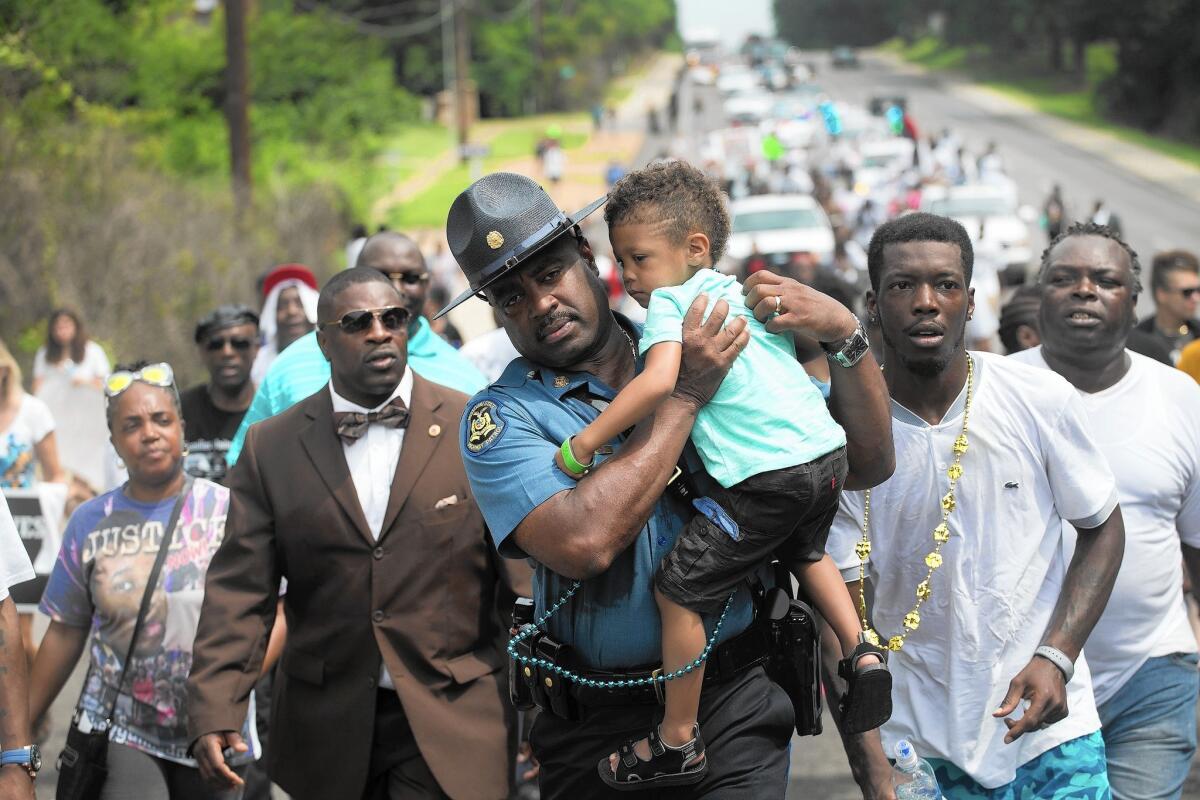 Capt. Ron Johnson of the Missouri Highway Patrol carries a demonstrator's child during a nearly five-mile march to mark the anniversary of Michael Brown's shooting death in Ferguson, Mo.