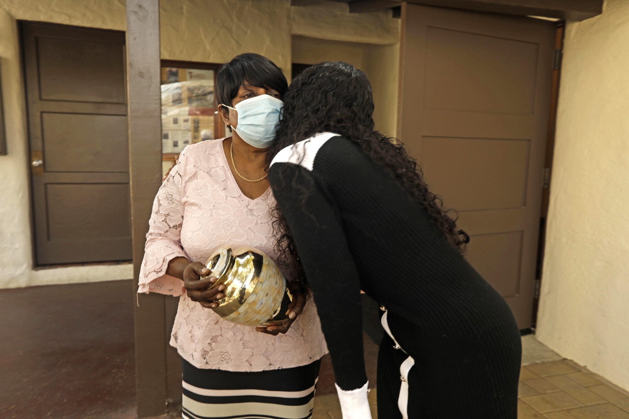 Margo Harris, left, holding the ashes of her brother Michael Wainwright, receives a hug from Sha'Ron Berry.