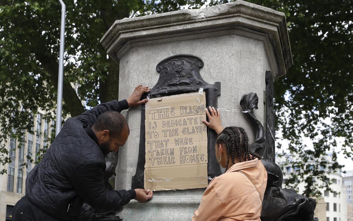 A A sign taped onto the statue of Edward Colston is dedicated to "the slaves that were taken from their homes"