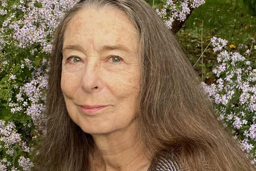 An older woman in a striped sweater standing in front of small pink flowers.