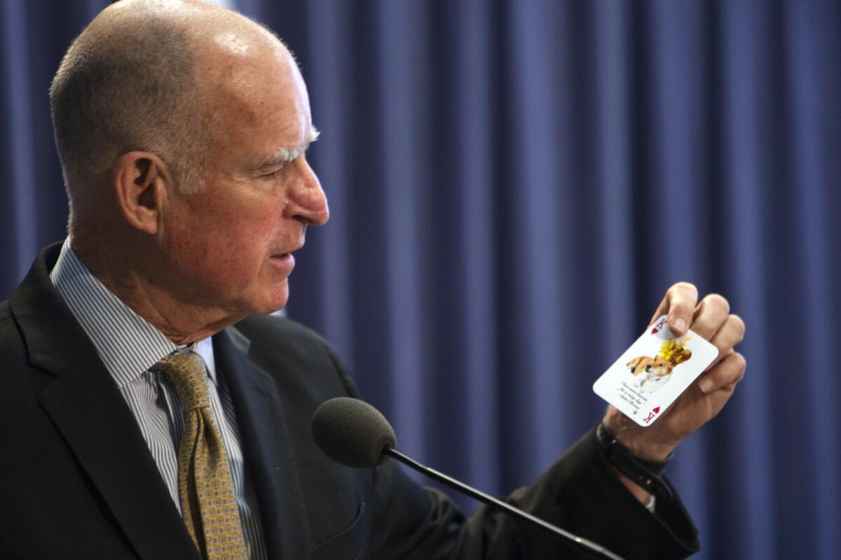 Gov. Jerry Brown holds a card which has a photo of his dog on the back and budget deficits on the front while announcing his revised 2014-2015 budget proposal during a news conference.