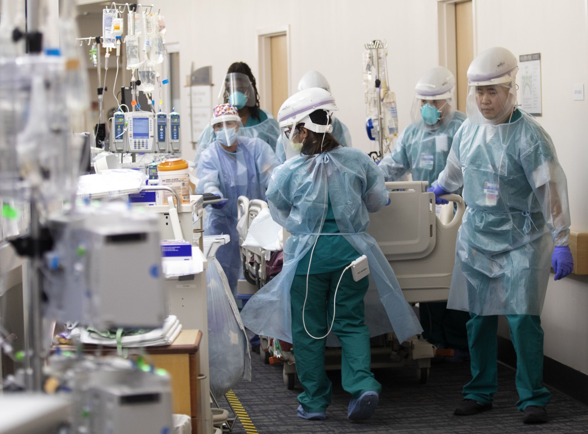 Hospital staff in protective gear move a gurney through the ER.