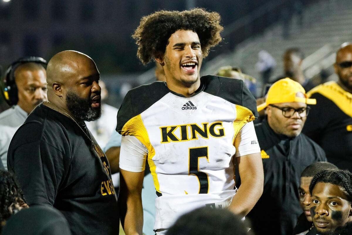 Detroit King quarterback Dante Moore flanked by several people.