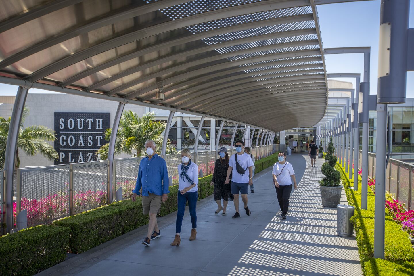 COSTA MESA, CA - JUNE 11: Shoppers wear protective masks while walking on The Bridge Of Gardens at South Coast Plaza as they reopen, requiring customers maintain a social distance and wear face masks at South Coast Plaza Thursday, June 11, 2020 in Costa Mesa, CA. Although not all stores in the upscale shopping center will resume operations, more than 110 merchants - including Apple, Macy's and Nordstrom - are opening their doors after being closed for three months amid the coronavirus pandemic. (Allen J. Schaben / Los Angeles Times)