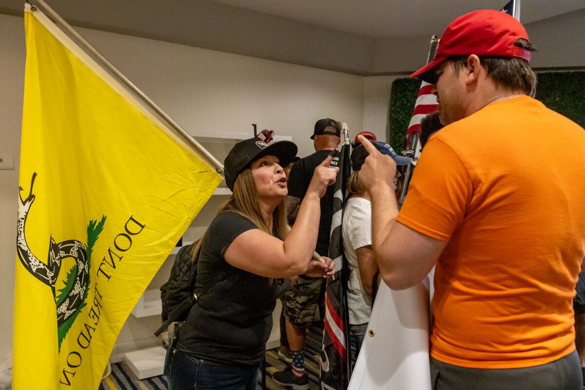 A man in a red hat and a woman holding a flag point fingers at each other.