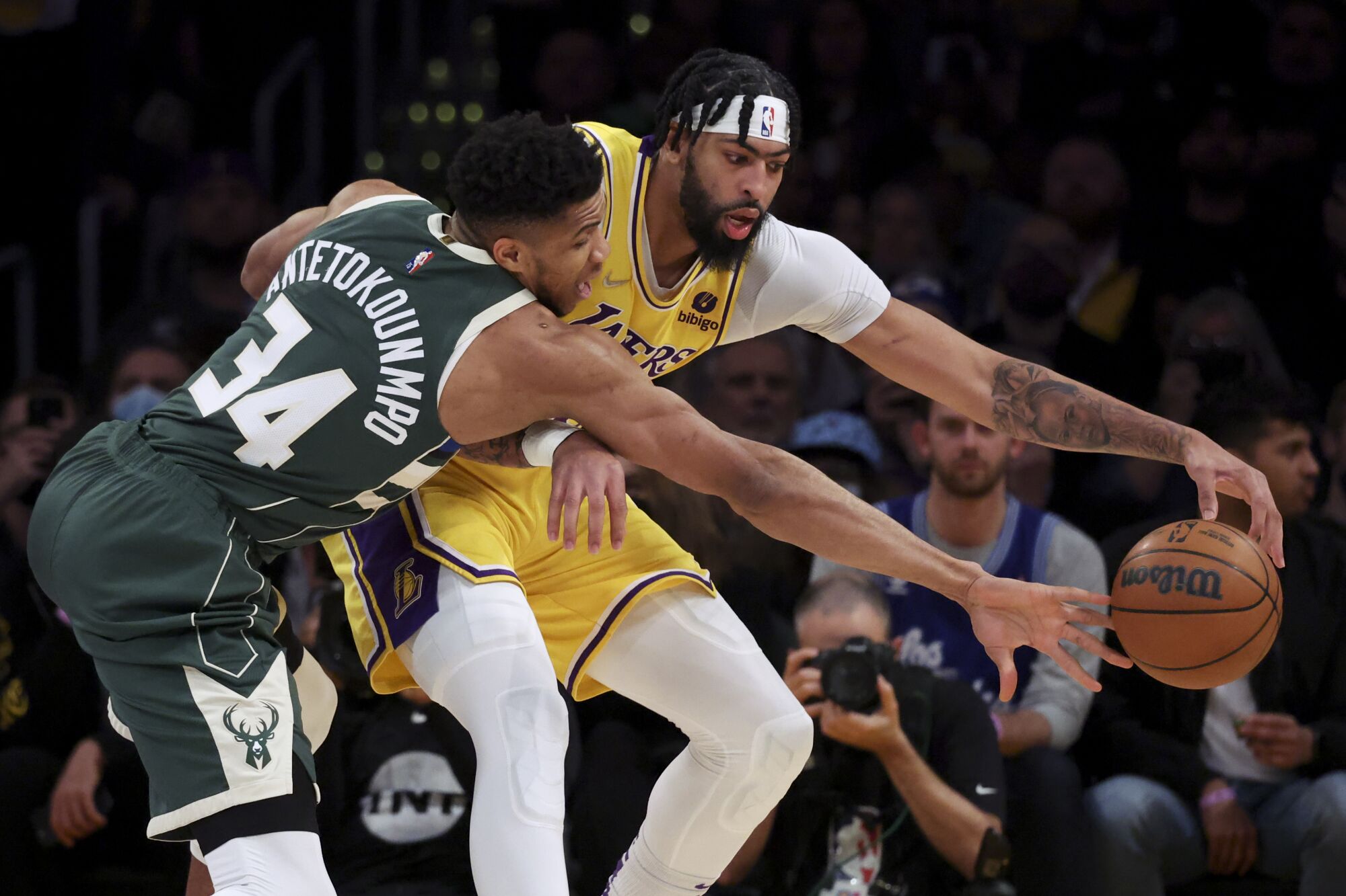 Lakers forward turns his side toward Bucks forward Giannis Antetokounmpo, who is reaching to try to steal the ball.