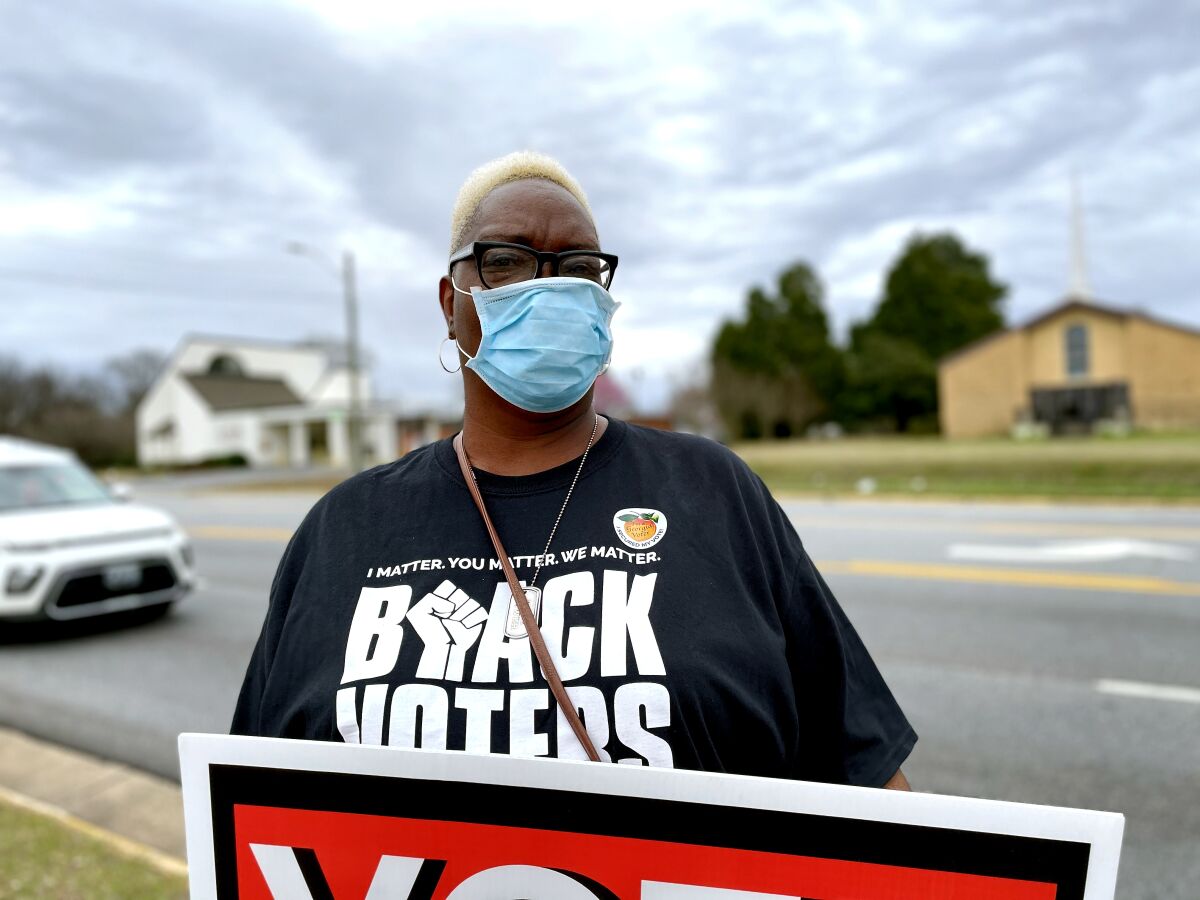 A woman in a Black Voters Matter shirt holds a sign.