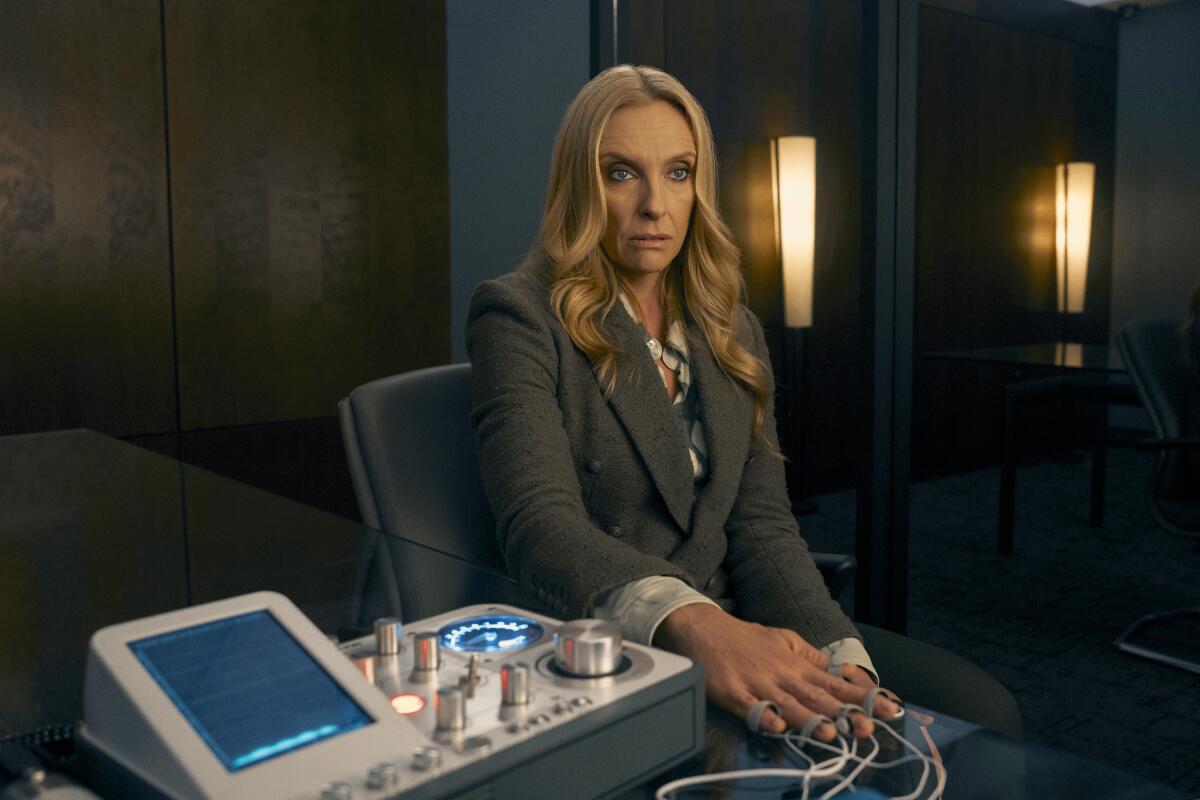 Toni Collette sits at a desk, her hand hooked up to a machine in "The Power.".