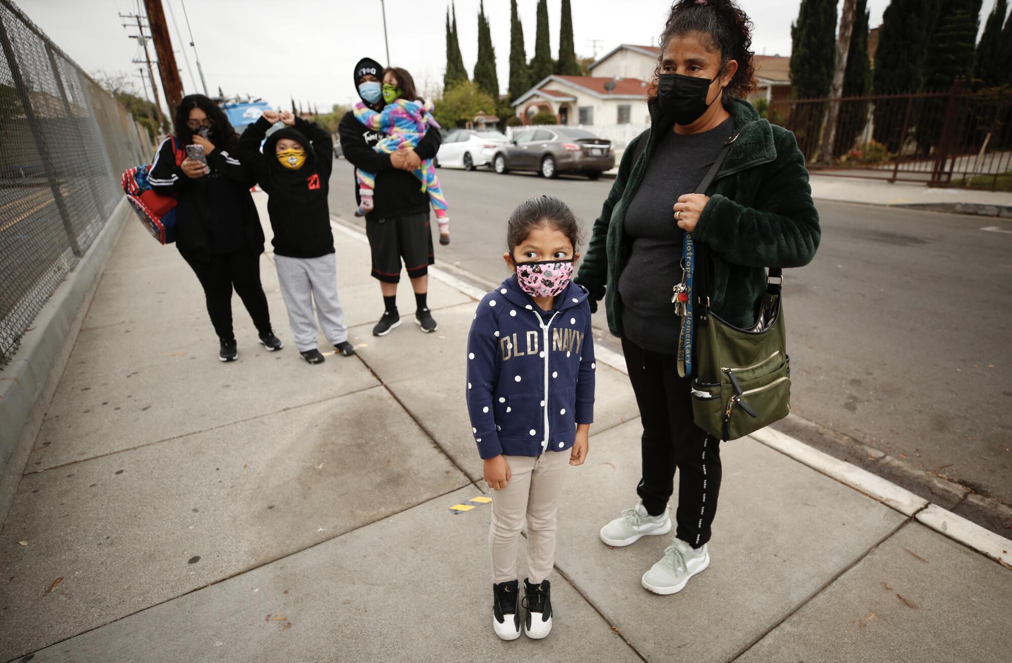 A girl stands next to her mother on a sidewalk outside her school.