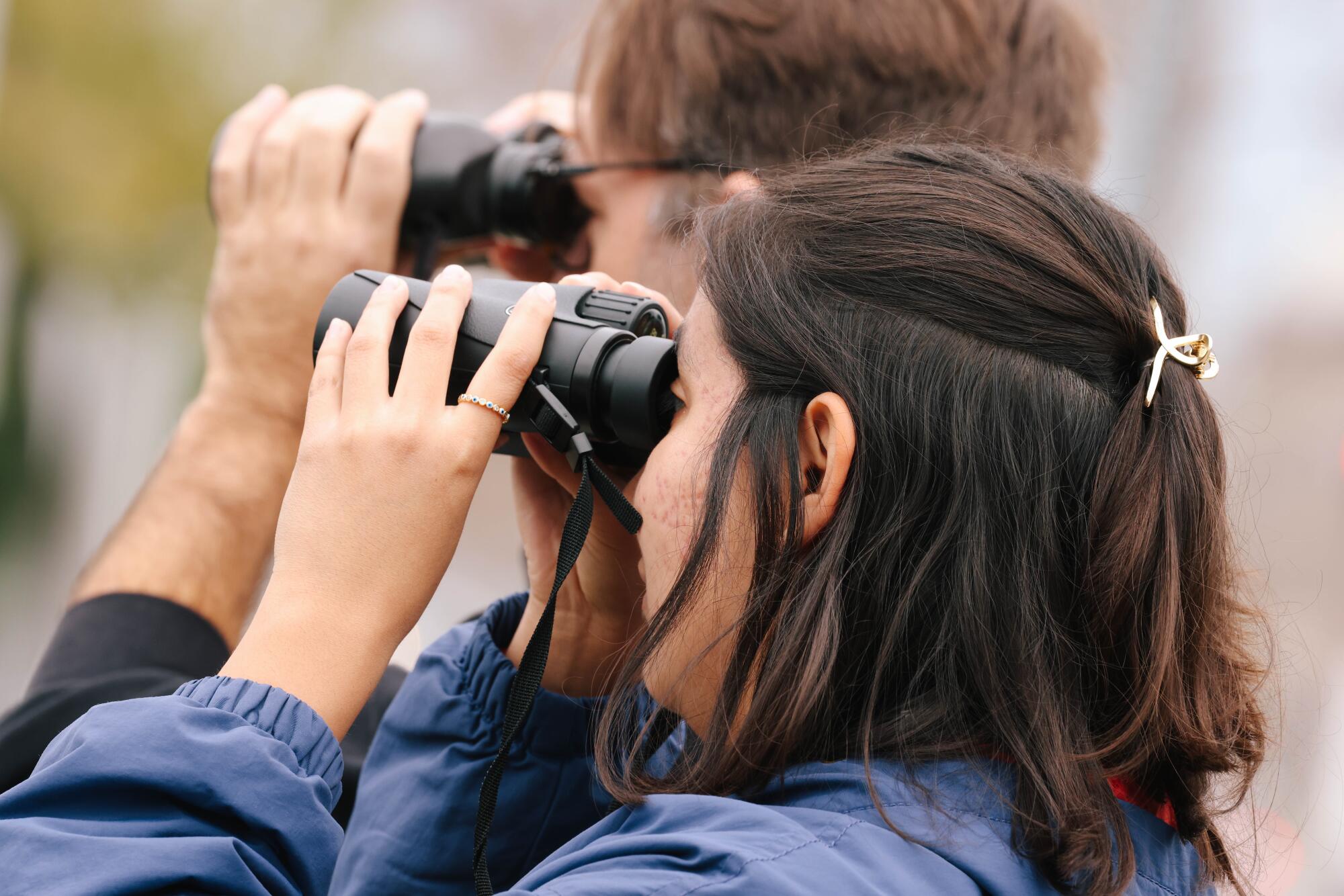 A man and a woman look through binoculars.