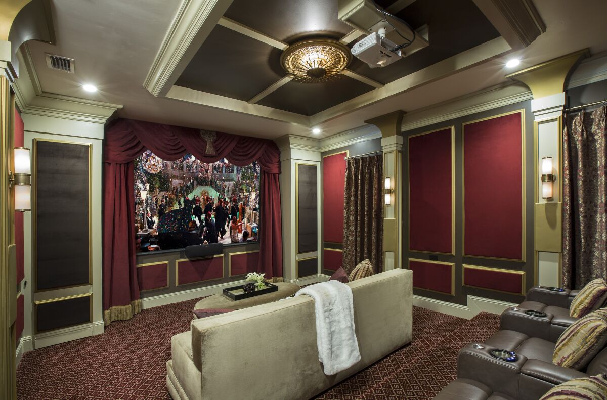 A home theater with red velvet on the wall panels and "champagne-hued velvet" on a big couch in the foreground.