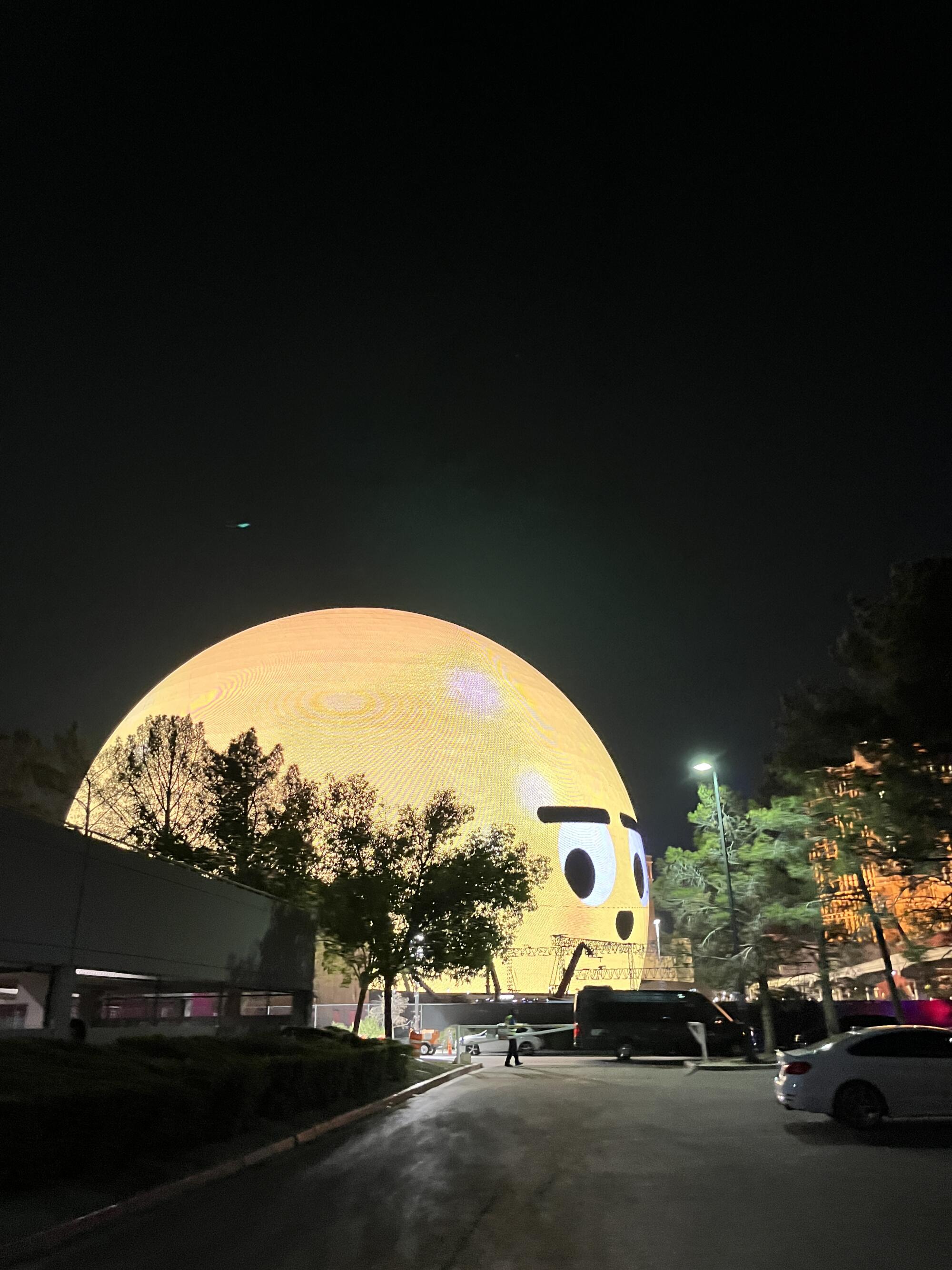 A spherical building covered in LED light is illuminated to resembled a bright yellow emoticon expressing surprise.
