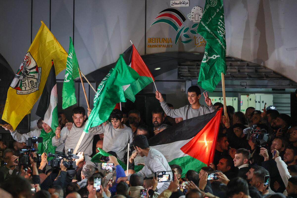Palestinian prisoners, wearing gray jumpers, celebrate with a crowd