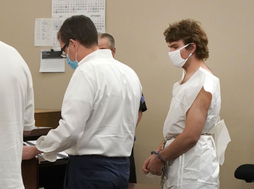 A man wearing a white mask and white paper smock, right, attends his arraignment in Buffalo City Court.