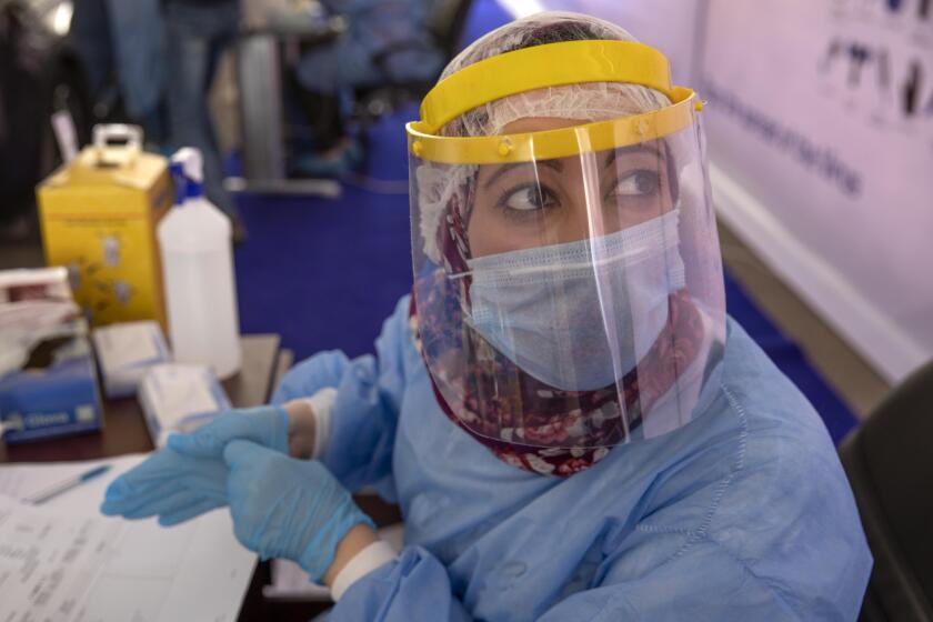 FILE - In this June 17, 2020 file photo, a health worker wearing protective gear prepares to take swab samples from people lining up in their cars to test for the coronavirus at a drive-through COVID-19 screening center at Ain Shams University in Cairo, Egypt. Coronavirus infections are surging in the country of 100 million, threatening to overwhelm hospitals. (AP Photo/Nariman El-Mofty, File)