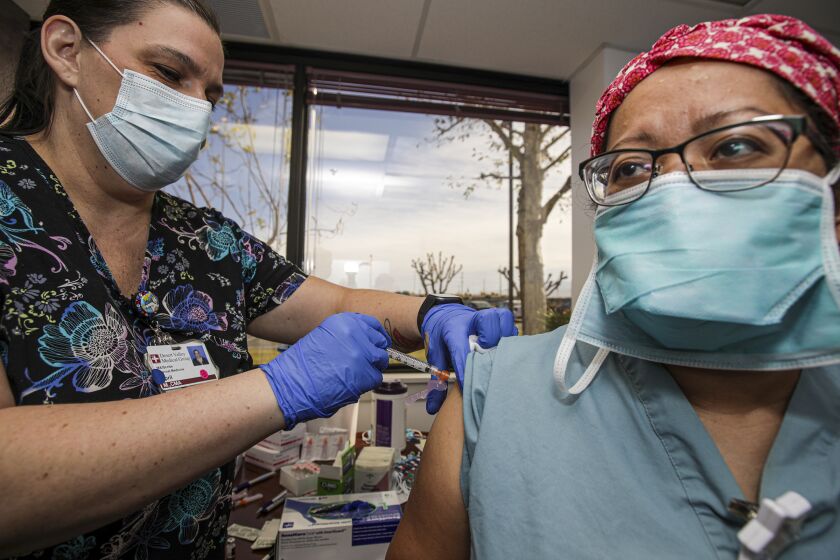 Victorville, CA - December 17: Medical assistant April Massaro, left, gives first dose of Pfizer BioNTech COVID-19 vaccine to nurse Alice Fallago at Desert Valley Hospital on Thursday, Dec. 17, 2020 in Victorville, CA. (Irfan Khan / Los Angeles Times)