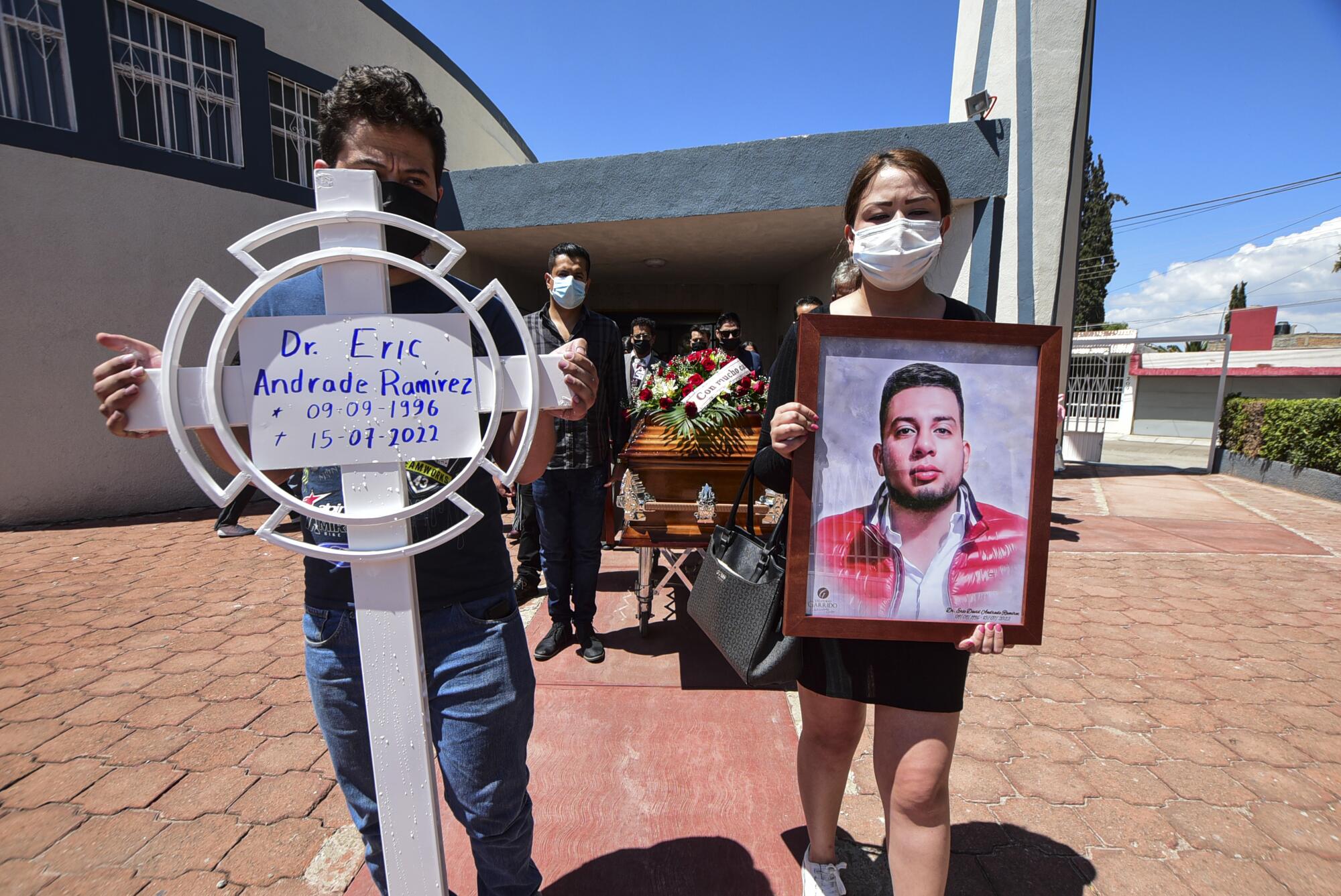 Mourners hold a sign and a portrait. 