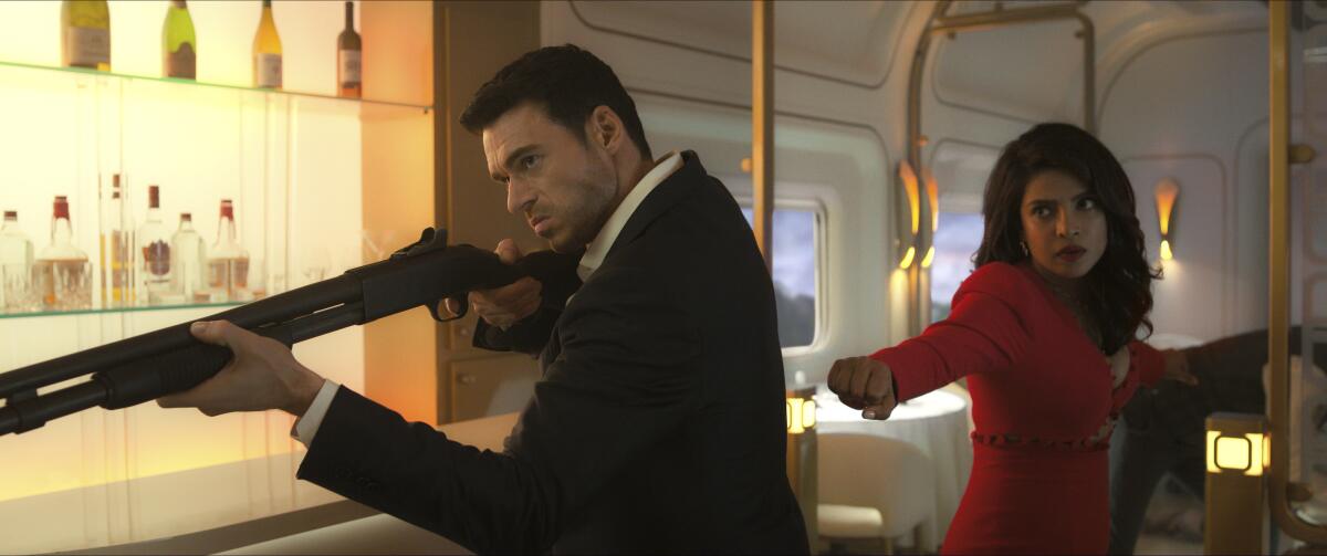 A man in a suit points a gun and woman in a red suit stands behind him with her arms in fighting stance.