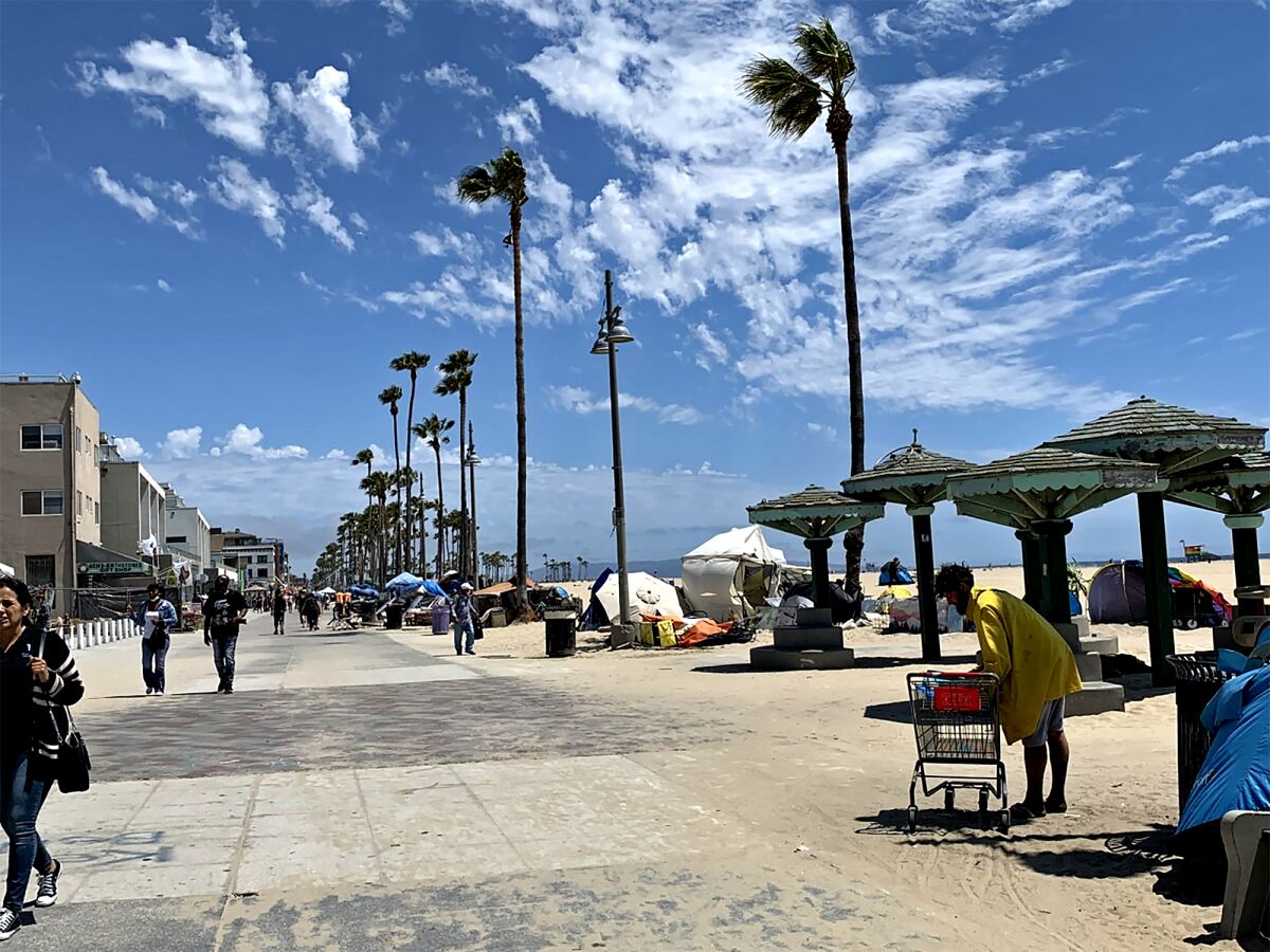 People walk on the Venice boardwalk under blue skies with white clouds.