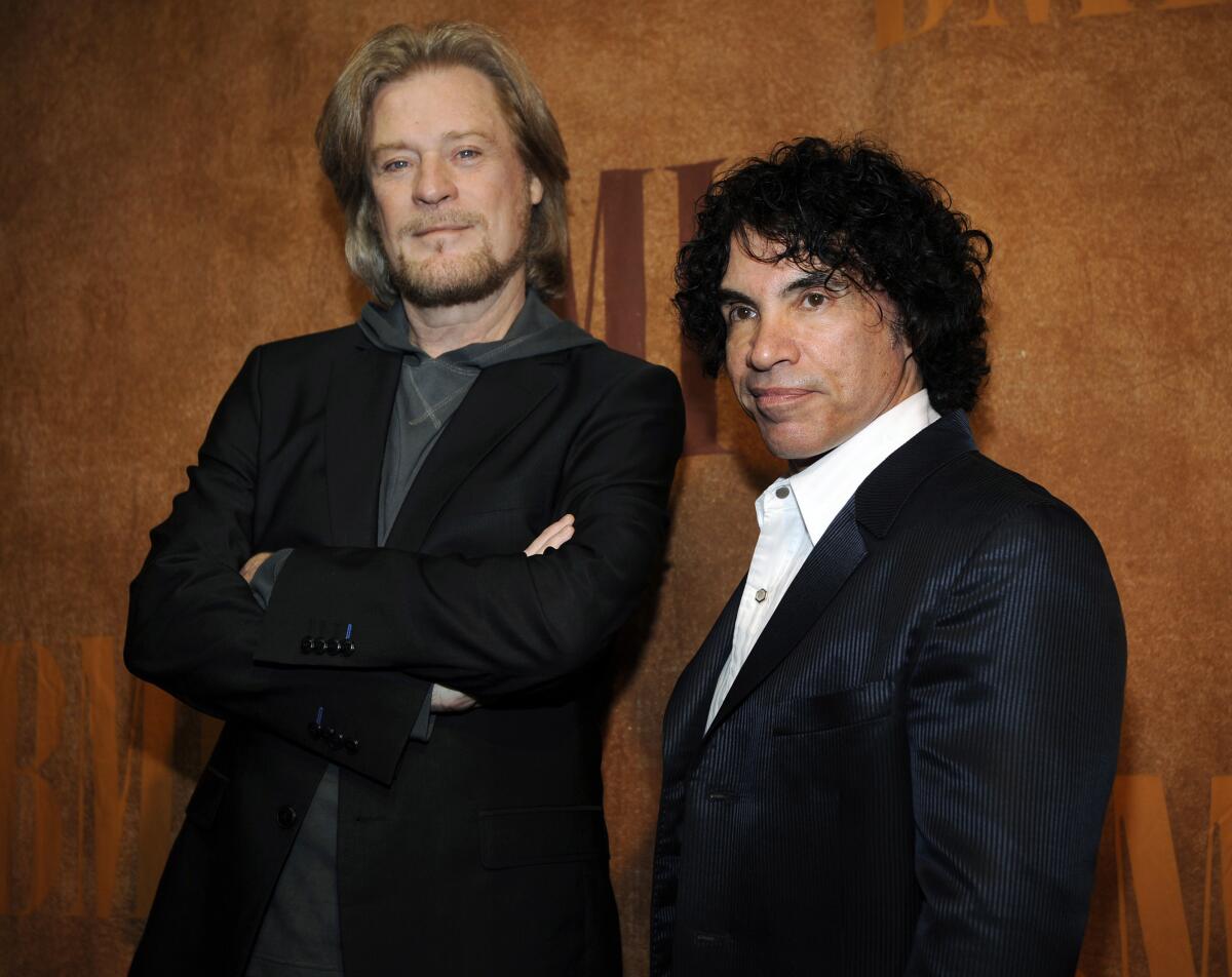 Daryl Hall crosses his arms in a hoodie and black blazer next to John Oates clad in a black jacket and white button-up shirt