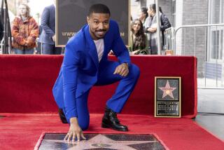 A man with short black hair wearing a blue suit and posing with a star on the Hollywood Walk of Fame.
