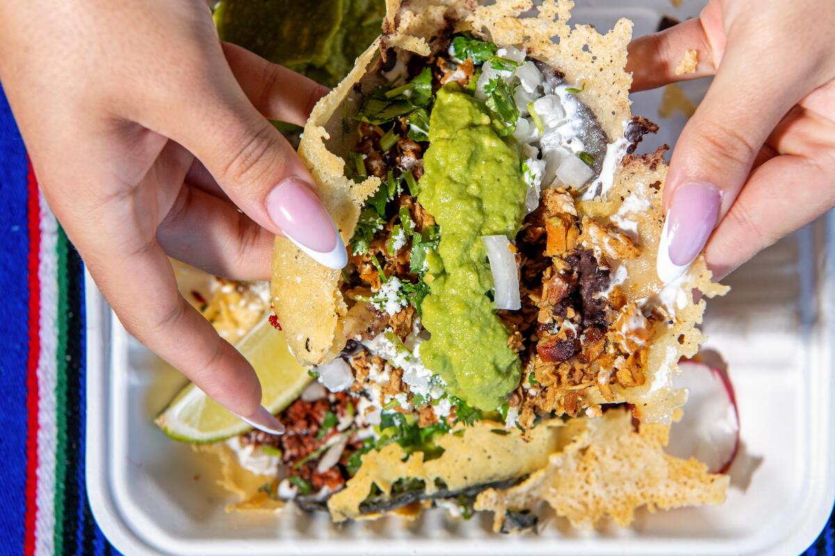 Hands split a taco to show its fillings, including guacamole.