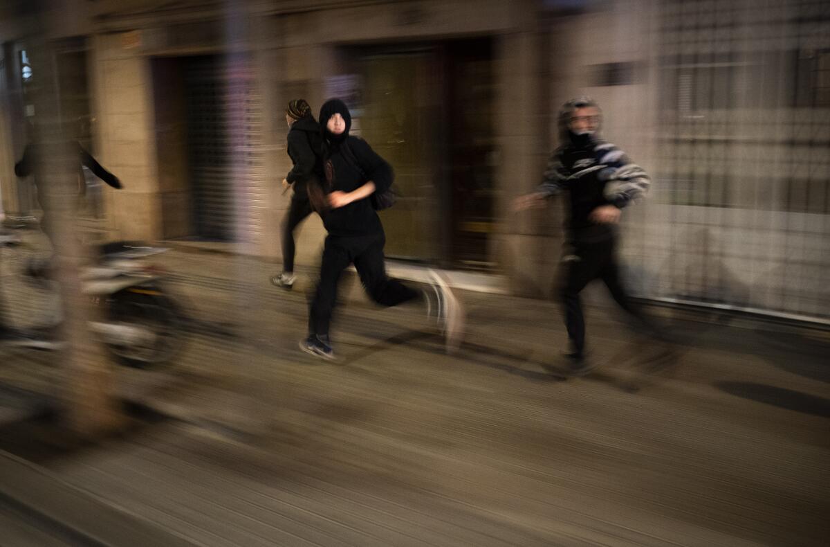 Protesters run away from police during clashes following a protest condemning the arrest of rap singer Pablo Hasél in Barcelona, Spain, Saturday, Feb. 27, 2021. Protests in support of the jailed rapper turned violent in Barcelona on Saturday with clashes between police and groups of mostly angry youths in the center of the Spanish city. (AP Photo/Emilio Morenatti)