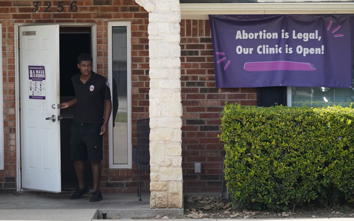 A security guard outside a building with a banner reading, "Abortion is legal, our clinic is open!"