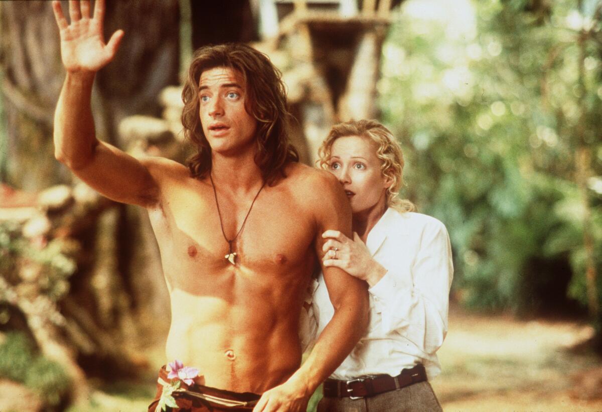 A blond woman in a white shirt clings to a shirtless man with long brown hair who is waving.