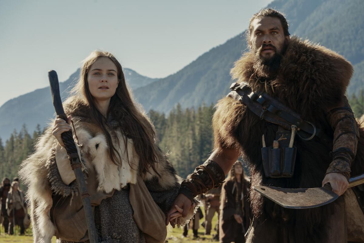 A man and a woman in furs hold hands before a mountain range in "See."