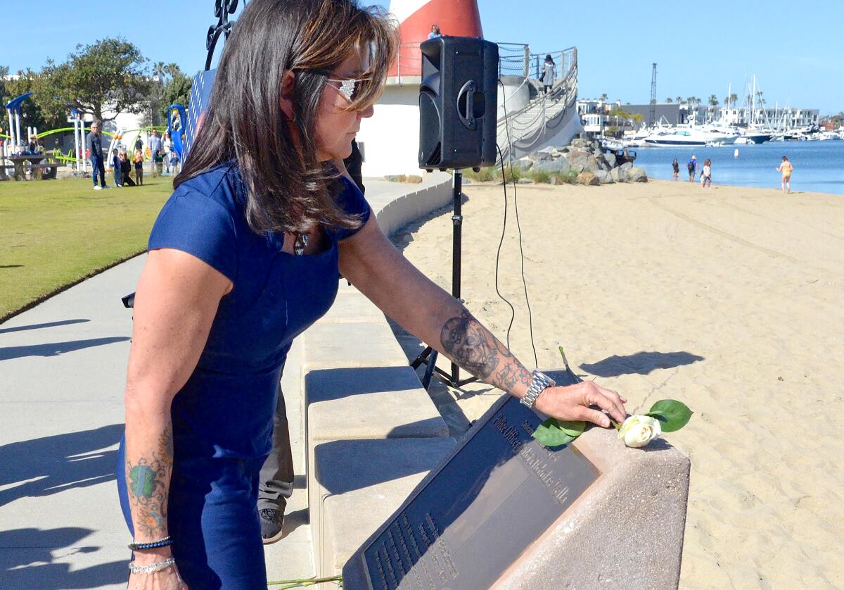 Kristi Vella places a white rose on the newly dedicated plaque installed on the seawall at Marina Park on Sunday.