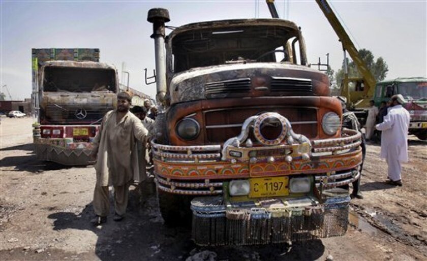 Pakistani drivers push a half burnt truck after militants attack at a terminal on the outskirts of Peshawar, Pakistan, on Sunday, April 12, 2009. Some 150 militants armed with rockets and automatic weapons attacked a northwest Pakistani terminal that lies along a key supply route used by U.S. and NATO troops, wounding three guards and torching eight cement trucks Sunday, police said. (AP Photo/Mohammad Sajjad)