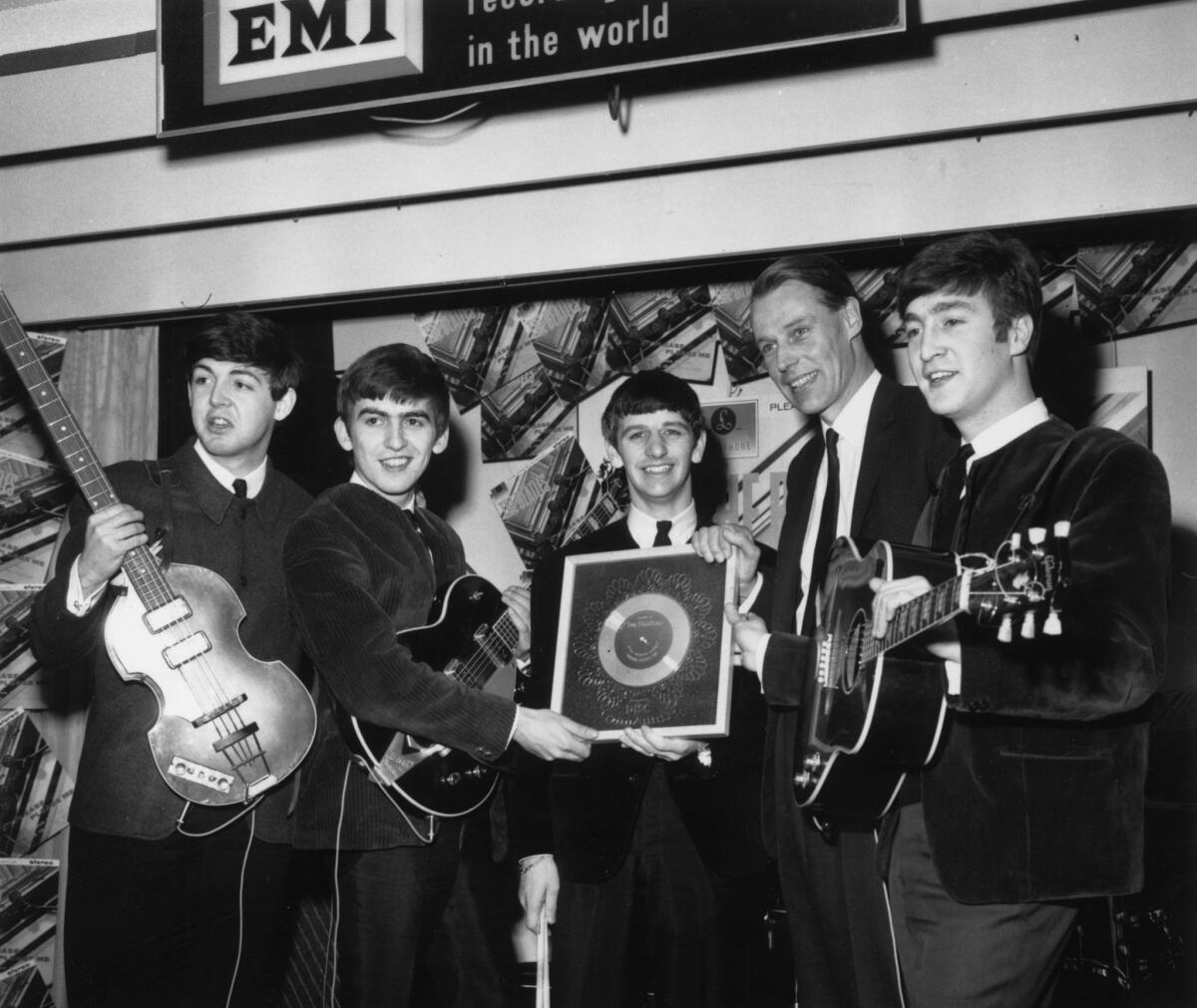 Beatles producer George Martin, second from right, stands with the group as they hold a silver disc marking their record sales in April 1963.