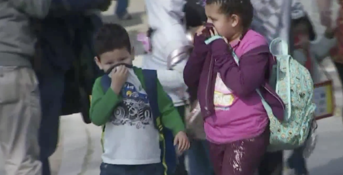 Children cover their noses after a jetliner dumped fuel on their school campus in Cudahy while making an emergency landing at Los Angeles International Airport.