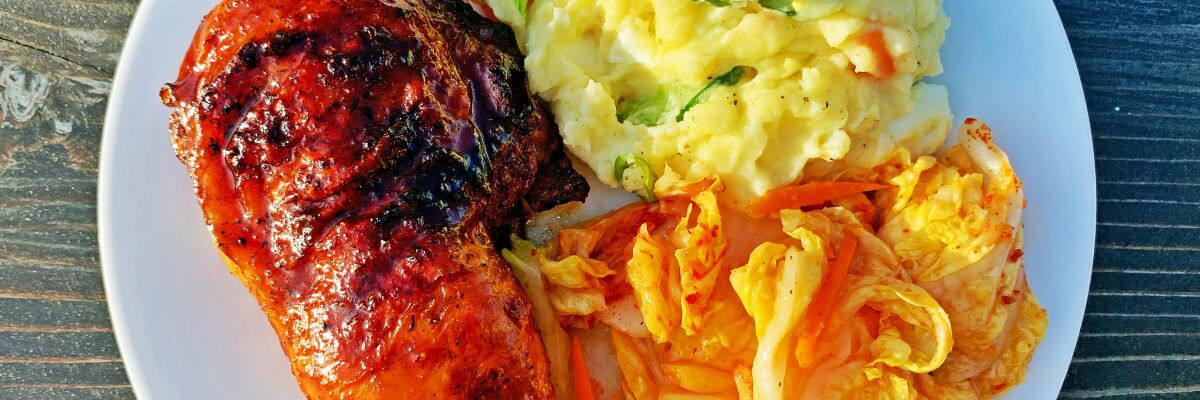 Gochujang-glazed grilled chicken on a white plate with with potato salad and kimchi.