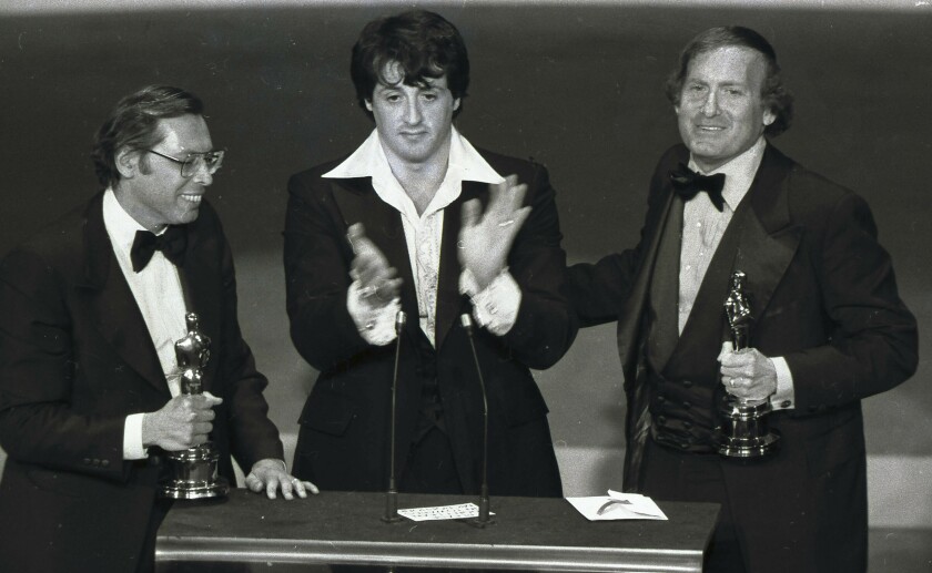 Three men in tuxedos stand on the stage