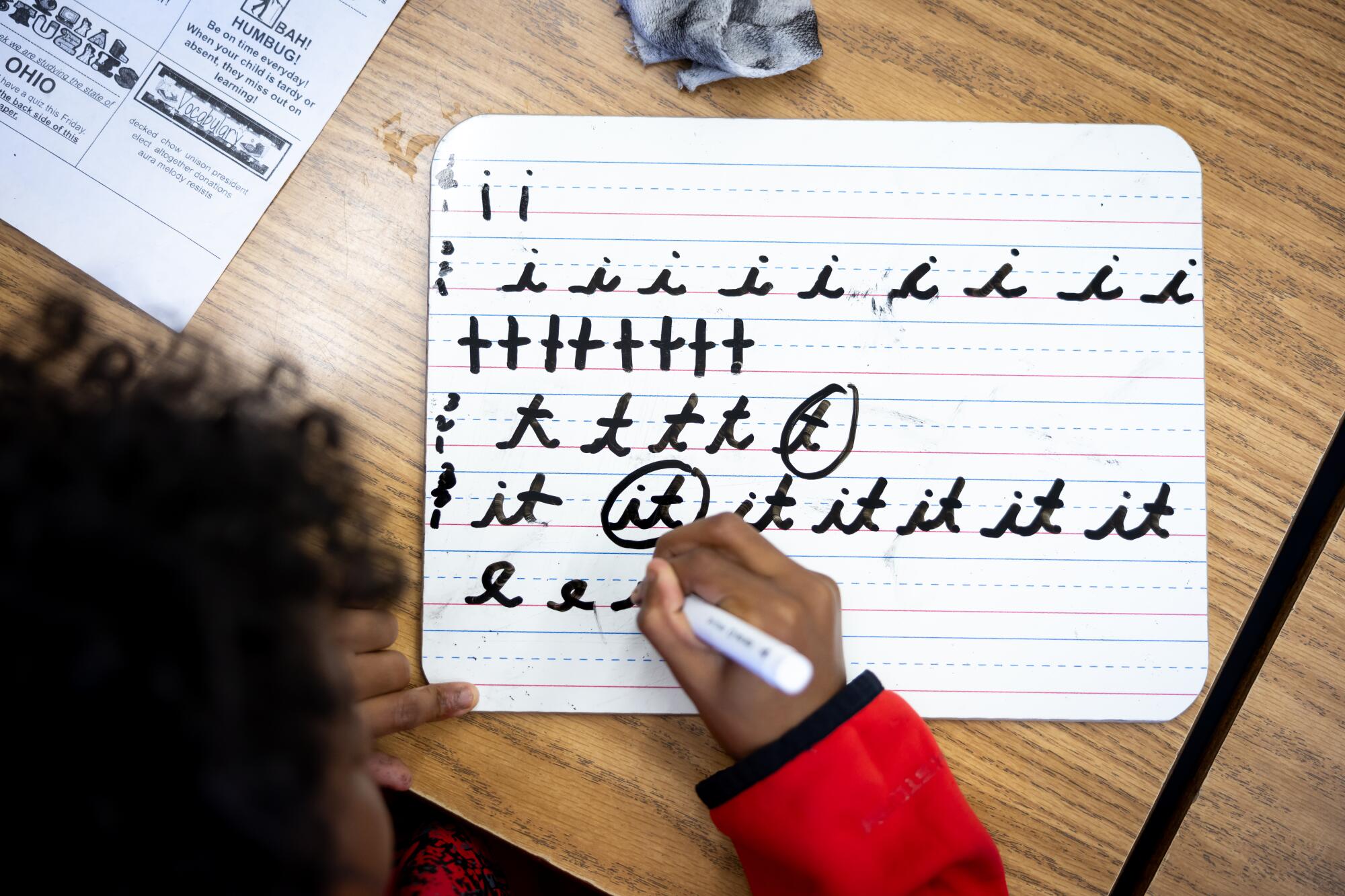 A fourth-grade student practices writing in cursive on lined paper. 