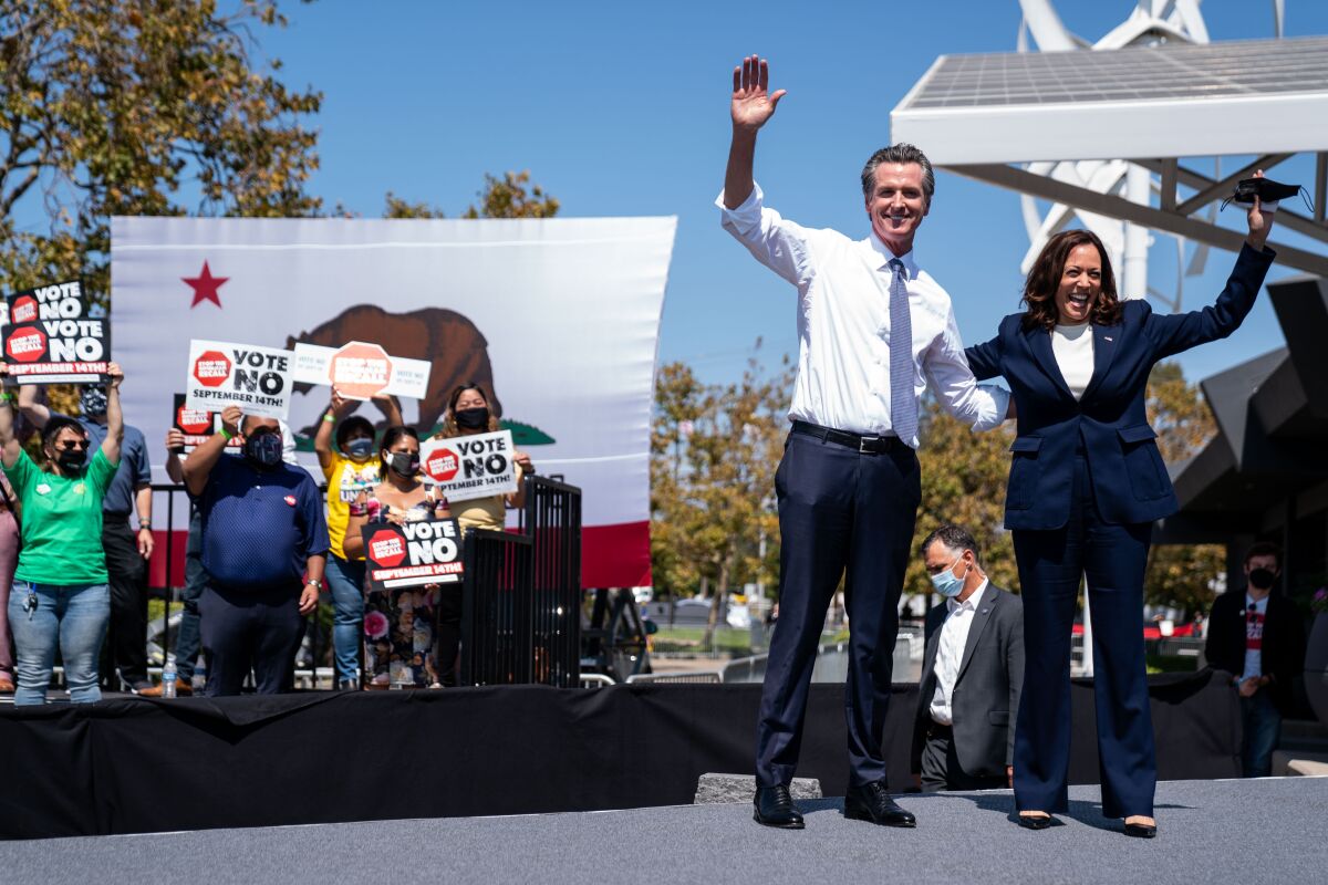Gavin Newsom and Kamala Harris wave onstage as supporters hold "Vote no" signs